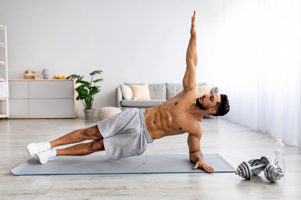 Jeune homme renforçant sa ceinture abdominale en faisant du gainage (planche latérale)